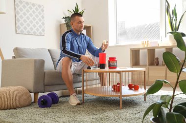 Sportif genç adam evde protein tozunu şişeye boşaltıyor.