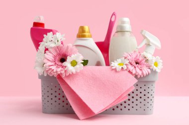 İçinde temizlik malzemeleri, aletler ve pembe arka planda bahar çiçekleri olan sepet.