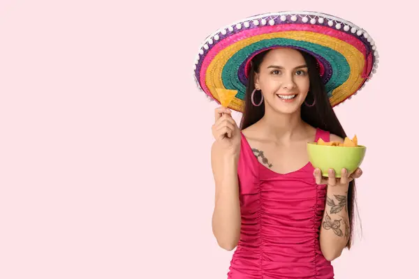 Stock image Beautiful young woman in sombrero hat with tasty nachos on pink background