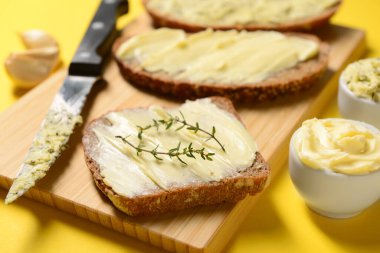 Tahta tahta ekmek dilimleri ve sarı arka planda taze tereyağı.