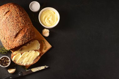 Siyah arka planda taze ekmek ve bir kase tereyağı olan ahşap tahta.