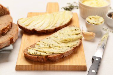 Tahta tahta ekmek dilimleri, taze tereyağı ve beyaz arka planda sarımsak.