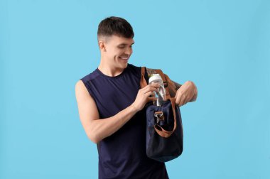 Mavi arka planda bir şişe su ve çanta taşıyan genç bir sporcu.