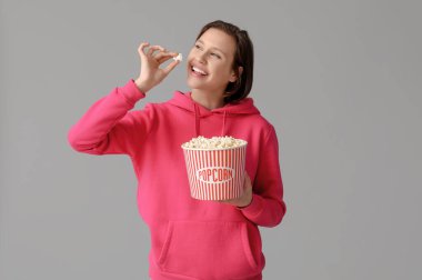 Gri arka planda patlamış mısırı olan mutlu, modaya uygun genç bir kadın.