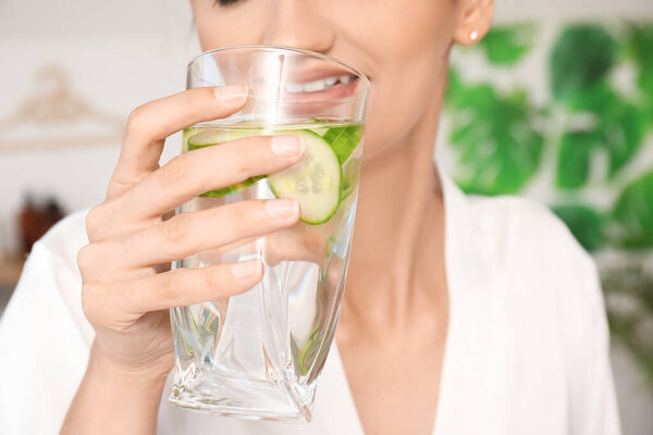 Young woman with glass of cucumber water at home, closeup