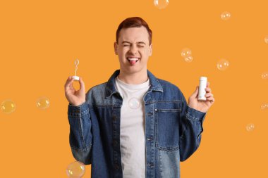 Genç mutlu adam turuncu arka planda sabun köpüğüyle oynuyor.