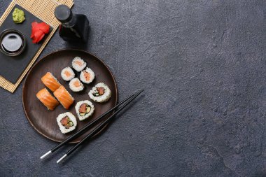 Soya soslu lezzetli suşi ruloları, yemek çubukları ve siyah grunge arka planda bambu hasırı.