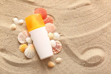 Bir şişe güneş kremi ve kumdaki deniz kabukları.