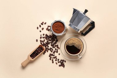 Fasulye, fincan ve bej arka planda ahşap kepçeli gayzer kahve makinesi.