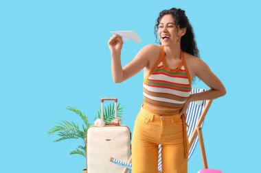 Genç Afro-Amerikalı kadın mavi arka planda kağıt uçakla oynuyor.