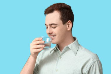 Yakışıklı genç adam mavi arka planda temiz su içiyor.