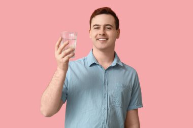 Handsome young man with glass of clean water on pink background