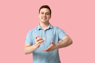 Handsome young man with glass of clean water on pink background