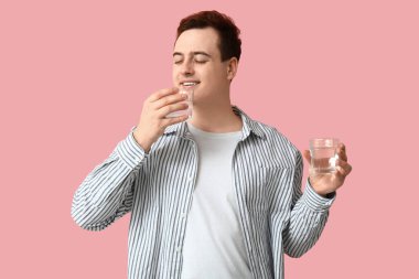 Pembe arka planda temiz su bardakları olan yakışıklı bir genç.