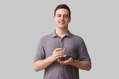 Gri arka planda bir bardak temiz suyu olan yakışıklı bir genç.