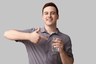 Yakışıklı genç adam gri arka planda bir bardak temiz suyu işaret ediyor.