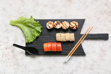 Lezzetli suşi ruloları, yemek çubukları ve beyaz grunge arka planda marul.
