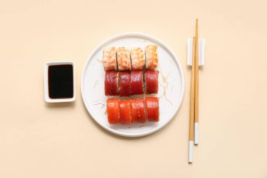 Lezzetli suşi ruloları, soya sosu ve bej arka planda çubuklar.