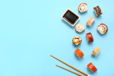 Lezzetli suşi ruloları, yemek çubukları ve mavi arka planda soya sosu.