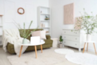 Yeşil kanepeli şık bir oda, kahve masası ve çiçek açan dallar, bulanık bir manzara.