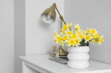 Lambanın yanındaki masada narsist çiçekleri olan vazo.