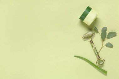 Yeşil arka planda bitkisel özü olan yüz masajı silindiri ve kremi