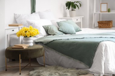 Nergisli vazo ve yatak odasının içindeki yeşil pouf üzerine kitaplar.