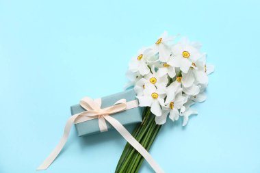 Bir buket güzel nergis çiçeği ve mavi arka planda hediye kutusu.