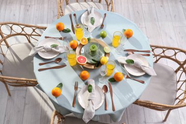 Oturma odasında turunçgiller, yanan mumlar ve açık mavi masa örtüsü üzerine portakal suyu olan güzel bir masa.