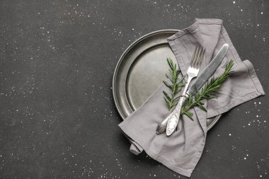 Siyah grunge arkaplan üzerinde peçete, çatal bıçak ve biberiye ile şık masa ayarları