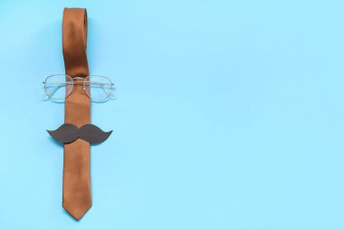 Mavi arka planda kağıt bıyıklı ve gözlüklü kravat. Babalar günü kutlaması. Üst görünüm