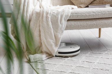 Evdeki koltuğun altındaki modern robot süpürgesi.