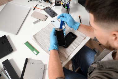 Servis merkezindeki masada cep telefonunu tamir eden erkek teknisyen.