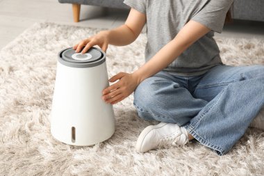 Genç bir kadın oturma odasının zemininde modern nemlendiriciyi açıyor.