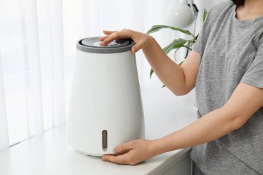 Genç bir kadının modern nemlendiriciyi açması. Odadaki çekmecelerin üzerinde, yakın plan.