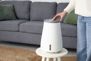 Genç kadın kanepede oturuyor ve oturma odasındaki modern nemlendiriciyi açıyor.