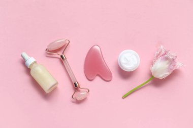 Yeşim silindirli gua sha, serum, kozmetik krem ve pembe arka planda lale çiçeği