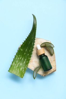 Mavi zemin üzerinde gerekli yağ ve taş şişesiyle taze aloe yaprağı.