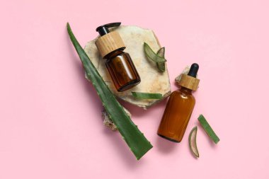 Kozmetik ürünleri şişeleriyle taze aloe yaprağı ve pembe arka planda taşlar.