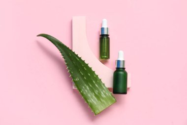 Pembe arka planda gerekli yağ ve alçı şişeleriyle taze aloe yaprağı.