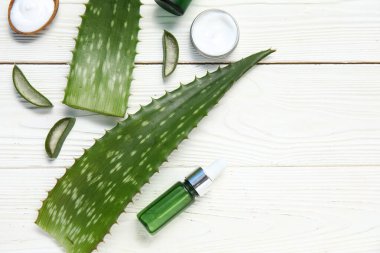 Aloe Vera yaprakları, kavanoz ve beyaz ahşap arka planda bir şişe kozmetik ürünü, yakın plan.