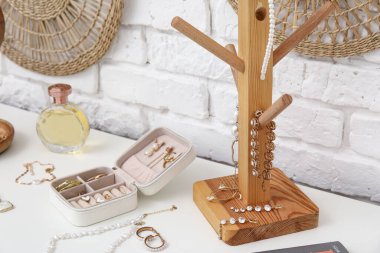 Beyaz tuğla duvarın yanındaki şifoniyerde farklı takılar var.