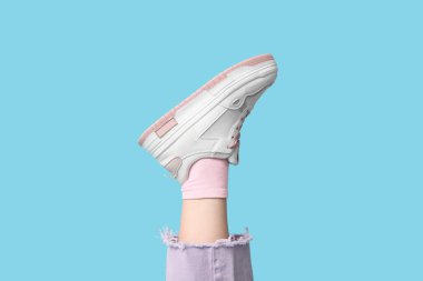 Mavi arka planda kot ve spor ayakkabılı genç bir kadın bacağı.