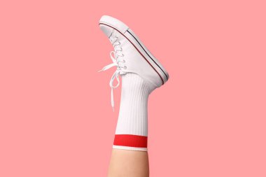 Çoraplı genç kadın bacağı ve pembe arka planda beyaz spor ayakkabılar.