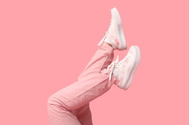 Pembe arka planda kot ve spor ayakkabılı genç kadın bacakları.