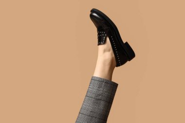 Pantolon giymiş genç bir kadın ve bej arka planda siyah deri ayakkabılar.