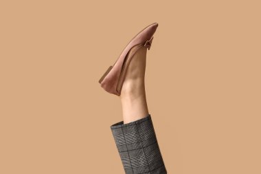 Pantolon ve alçak ayakkabılı bej arka planda fiyonklu genç kadın bacağı.