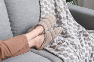 Oturma odasındaki kanepede rahat terlikler içinde kadın bacakları.