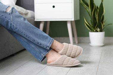 Şık terliklerle kadın bacakları odada yerde.