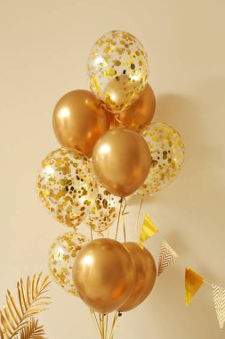 Evdeki bej duvarın yanında bayraklı güzel altın balonlar.